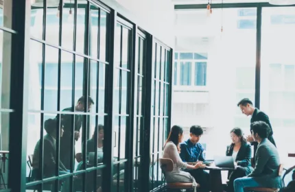 Team of professionals seated around a table working on laptops and documents in a glass-walled office, representing expert support for managed review and document production processes.