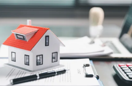 Model house, pen, and contract paperwork on a desk representing property and casualty insurance supported by BH Technologies.
