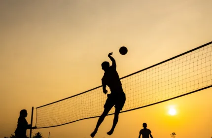 A backlight athlete jumps to volley a ball back over a net at sunset